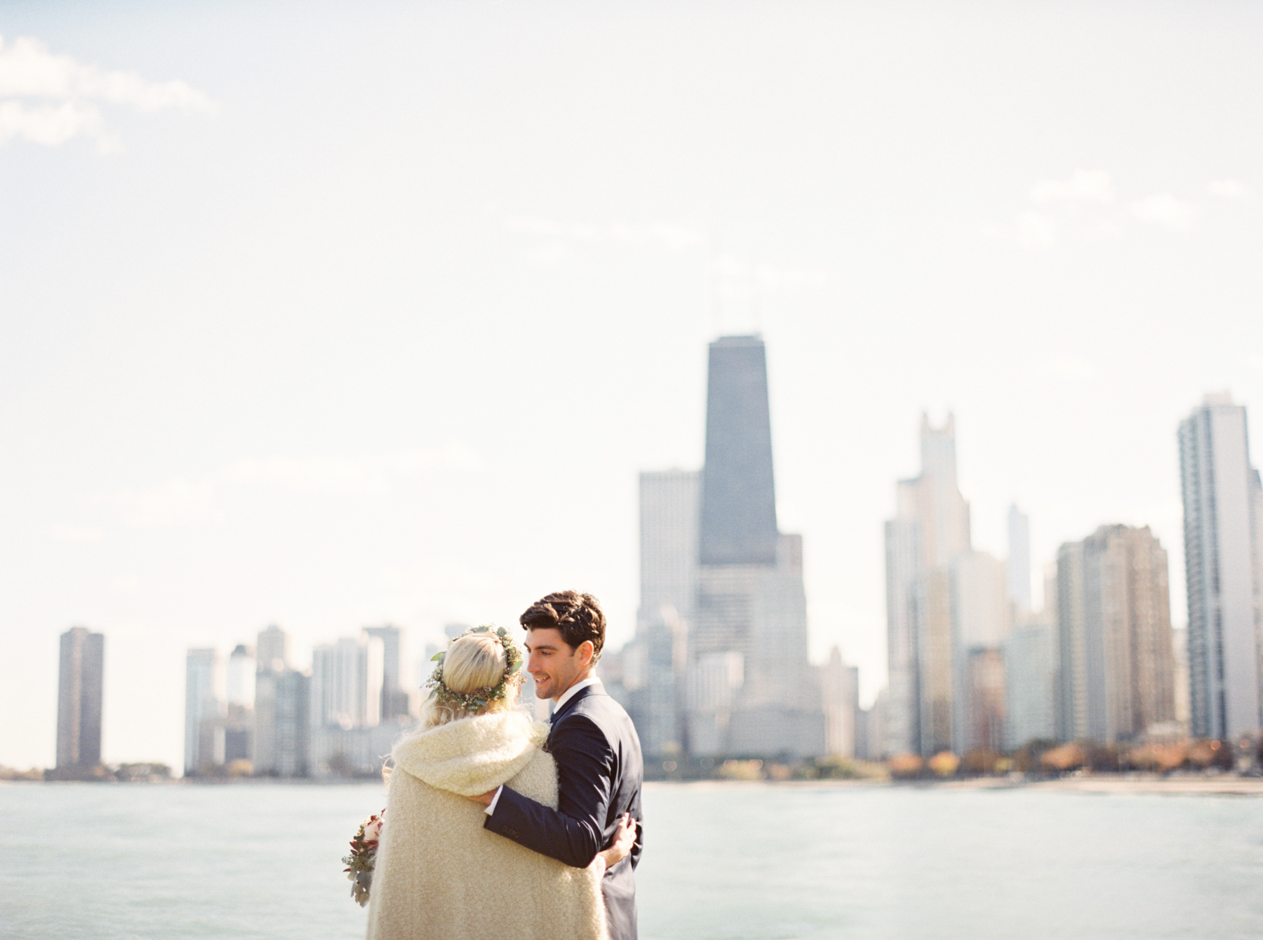 bride and groom walking along river with chicago skyline in background Chicago Wedding Photographer