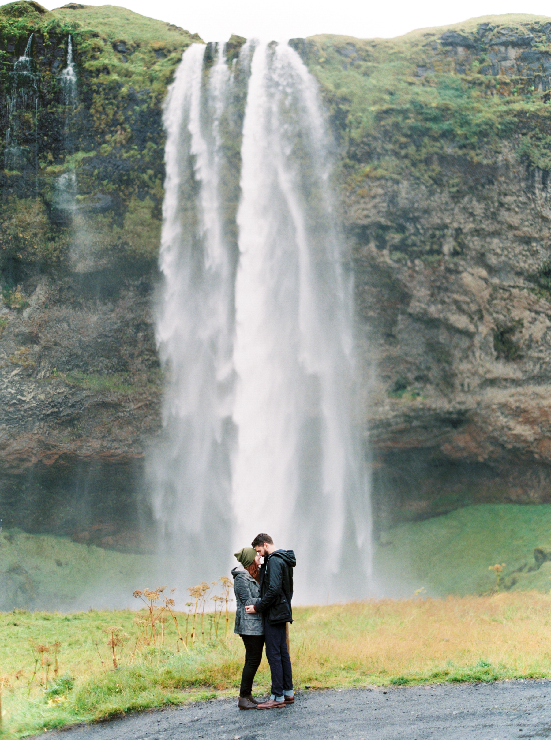 two photographers embrace in front of beautiful waterfall in Iceland