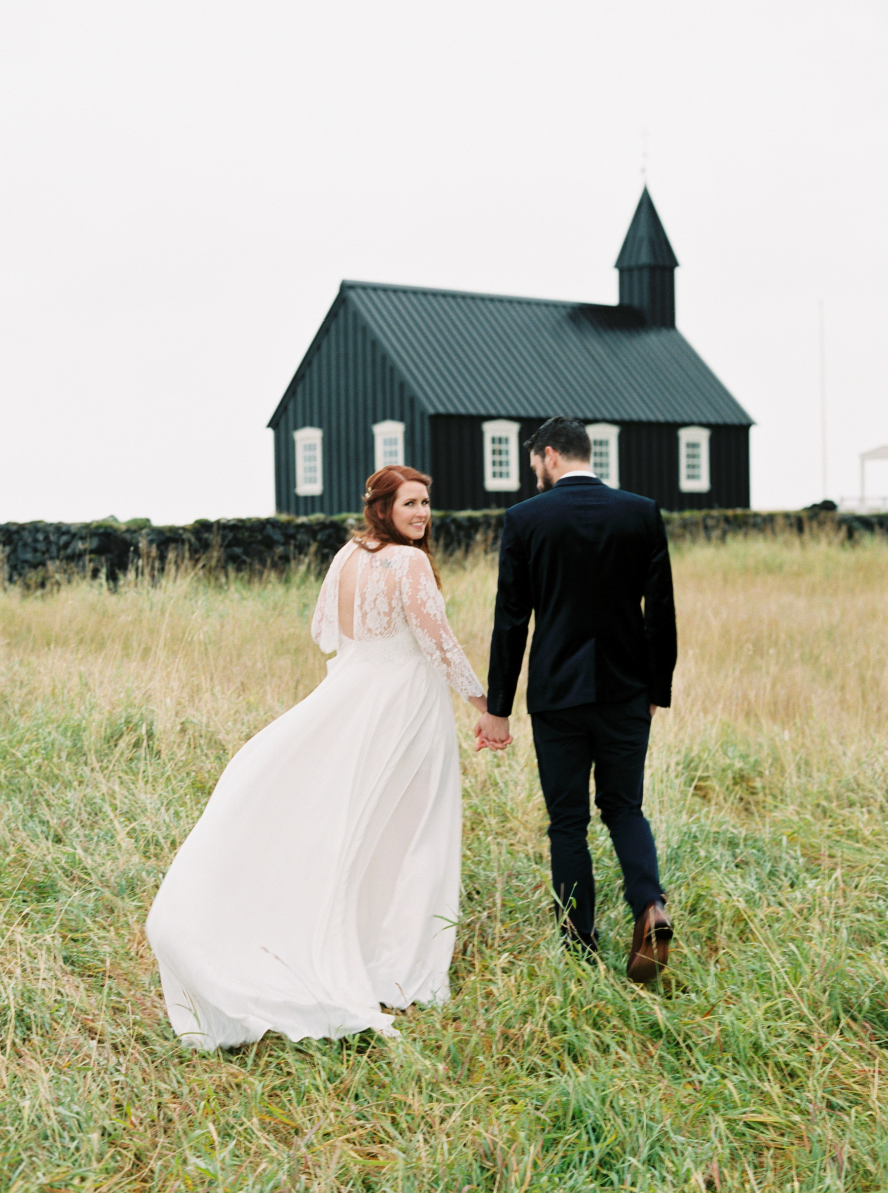 bride and groom in field next to black church before Iceland Wedding At Hotel Budir & the Black Church