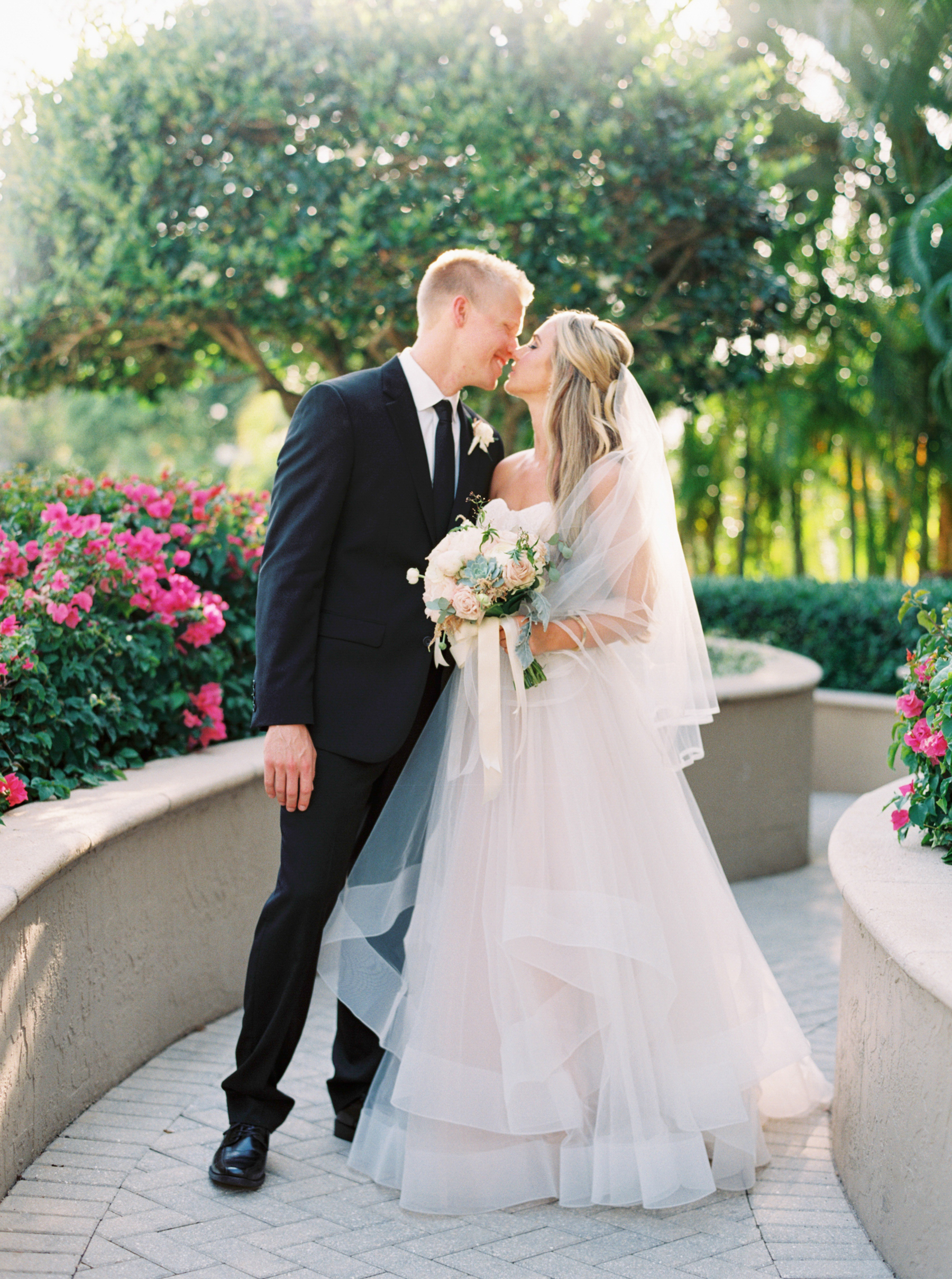 bride and groom touches noses in garden of pink flowers at Naples Florida Wedding 