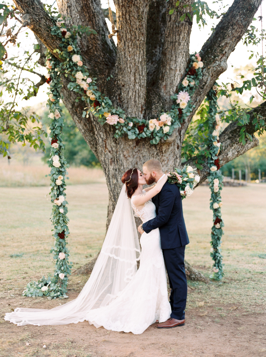 bride and groom kissing under large tree with floral altar at Vinewood Plantation Wedding in Newnan GA