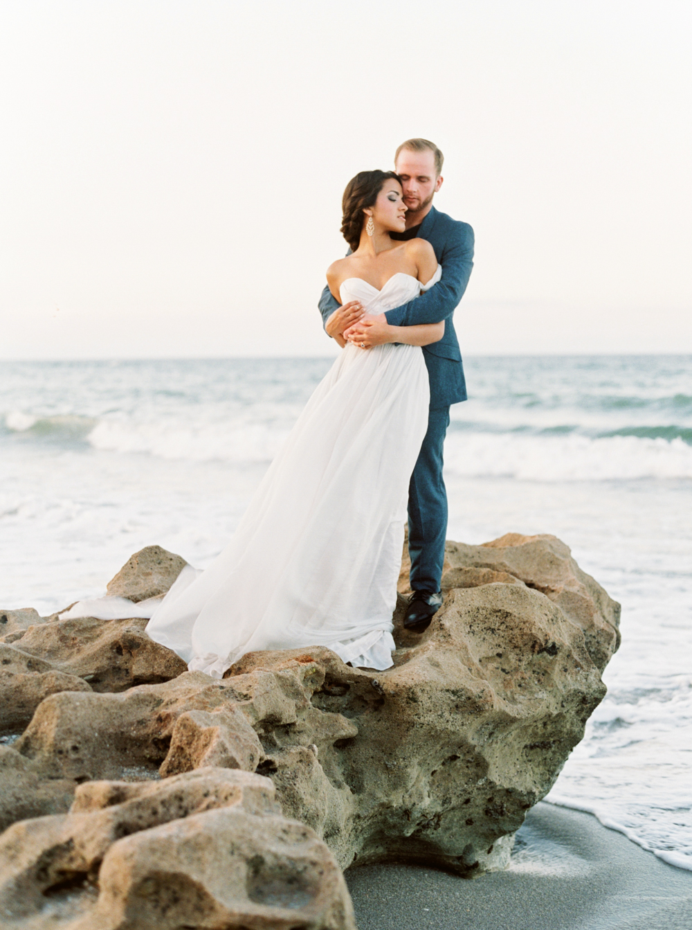 bride and groom embrace on rock perched above the Florida waves in Styled Wedding Shoot with Elleson Events