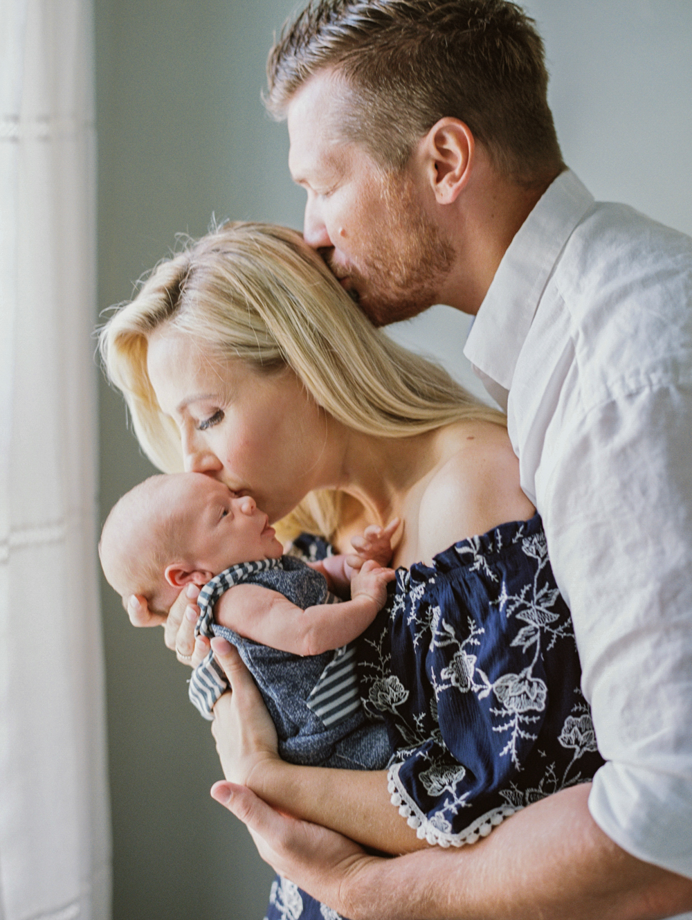 mom kisses newborn while dad kisses mom during Maternity and Newborn Sessions