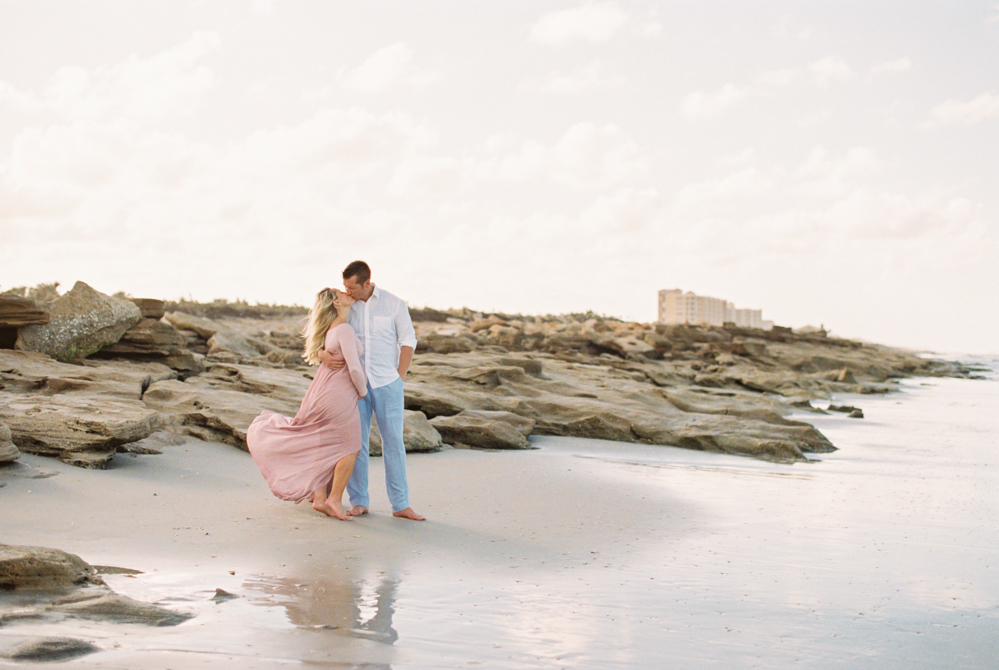 expecting parents kiss on rocky beach during Maternity and Newborn Sessions